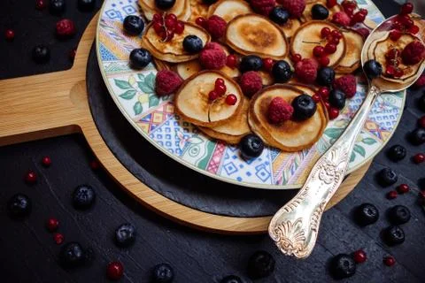 Small pancakes with berries on a patterned plate with silver spoon in rustic Stock Photos
