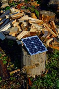 A small panel of solar cells on an old stump on the background of chopped fir Stock Photos