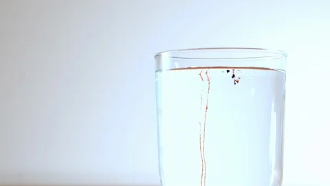 Small particles of red substance fall into a transparent glass with water 库存影片 116050847