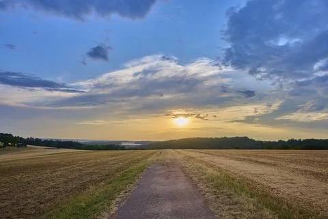Small path leads through a field at sunset surrounded by a dramatic sky, summer, Stock Photos