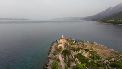 Small Peninsula Lighthouse and Mountain Coastline in Hazy Morning Light Stock Footage 346630559