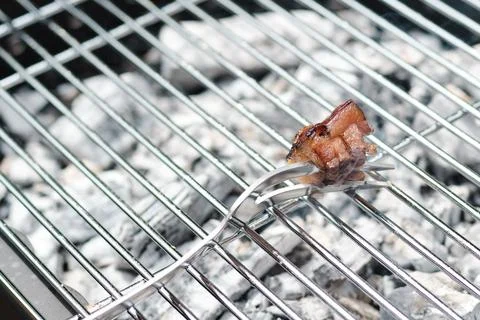 A small piece of bacon held on a fork over hot barbecue grill Stock Photos