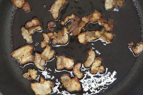 Small pieces of bacon are cooked in a pan. Top view. Stock Photos