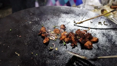 Small pieces of chicken being fried on a big frying pan with onion for Stock Footage 122562797
