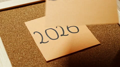 A small pile of peach sticky notes on cork, the top one marked 2027 in black Stock Footage 347510185