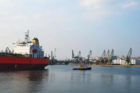 A small pilot ship leads a large red cargo ship at the seaport Stock Photos