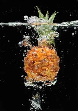 Small pineapple falling in water on black Stockfoto's