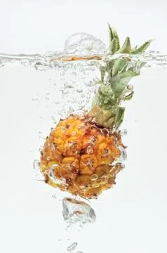 Small pineapple falling in water on white Stock Photos