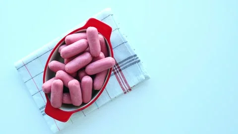 Small pink sausages in a red ceramic bowl on a white table, on a tea towel. Stock Footage 333031896