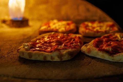 Small pizzas baking near flame inside stone oven Stock Photos