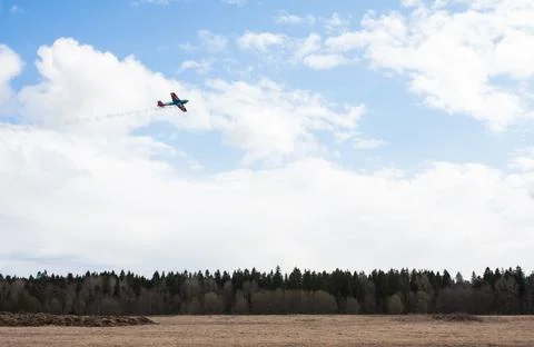 Small plane flies over field and forest Stock Photos