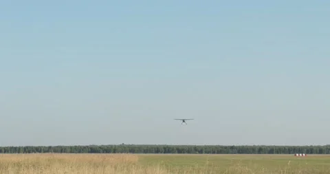 A small plane with a hanging cable for towing a glider lands on a field. Video stock 160726771
