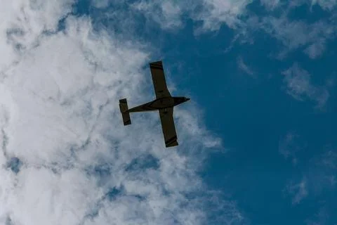 Small plane under the white clouds. Bottom view. Stock Photos