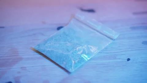 Small plastic bag containing white powder, possibly drugs, on a wooden table Vidéo 335196599
