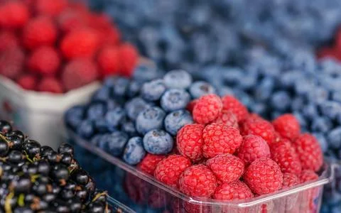 Small plastic boxes with blueberries and raspberries displayed on food mark.. Stock Photos