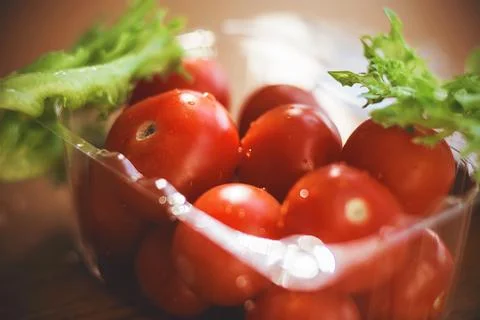 In a small plastic container are ripe cherry tomatoes, and next to them green Stock Photos