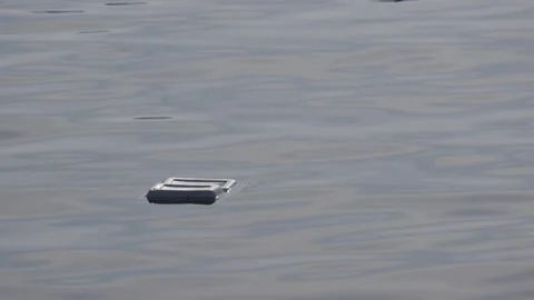 A small plastic container floats on a calm water surface with gentle ripples. Ma Vídeo Stock 343041132