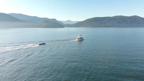 A small pleasure craft towing a dingy with Howe Sound and the mountains in the Stock-Footage 128740767