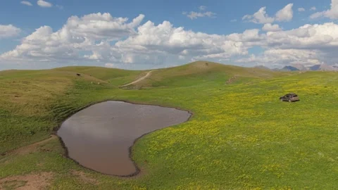 Small pond reflecting clouds in green meadow with suv parked Video stock 312448848