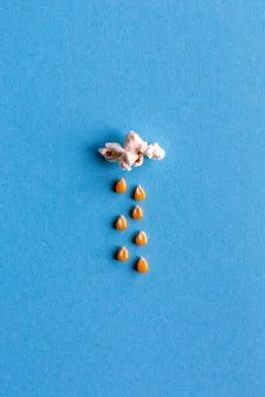 Small popcorn cloud with rain made out of corn kernels on blue background 스톡 사진