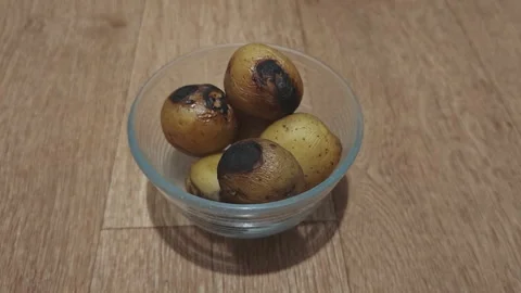 Small potatoes burnt during baking process sitting in a clear glass bowl Stock Footage 347735657