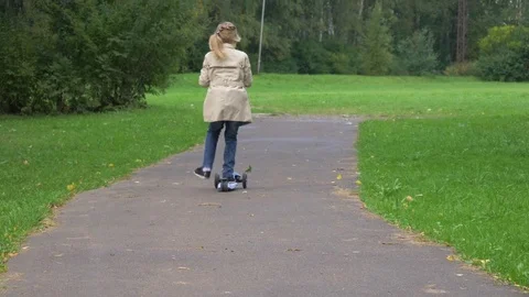 Small preschooler caucasian girl in jacket is riding on kick scooter on path Stock Footage