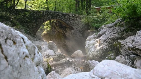 Small pristine Alpine creek flowing between rock boulders under old bridge Stock Footage 137155327