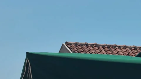 Small propeller airplane flies low above tiled rooftops under a clear blue sky Stock Footage 344901655