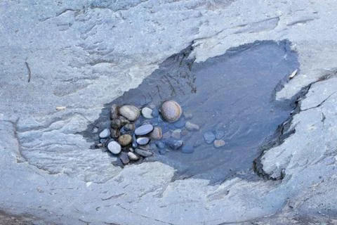 Small puddle with pebbles isolated in grey rock formation Stock Photos