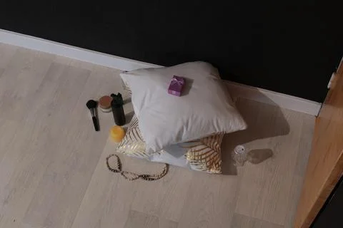 Small purple gift box on white pillow with makeup and jewelry on floor 스톡 사진