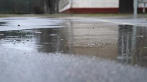 Small raindrops falling into big puddle on road. Rain drops splashing on water Stock Footage 297058889