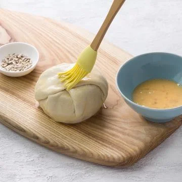 Small raw pie smeared with egg before baking surrounded by two bowls with a.. Stock Photos