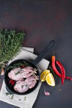 Small raw quals with some spice ready for cooking on black round pan . Foto stock