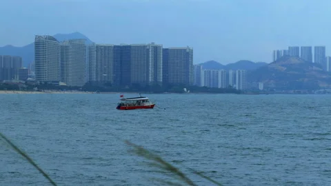 Small red boat on blue sea, coastal city skyline with modern apartments, peacefu Stock-Footage 332668657