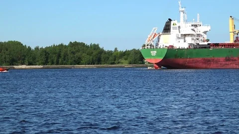 Small red boat sails behind tremendous vessel along river Stock Footage 113090629