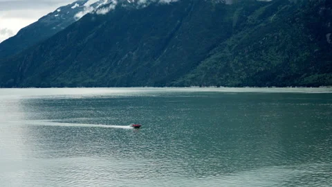 Small red boat speeding across fjord below mountains in Alaska Stock-Footage 348018748