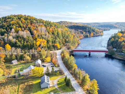 Small red bridge elegantly spanning a serene river in a vibrant autumn forest Stock Photos