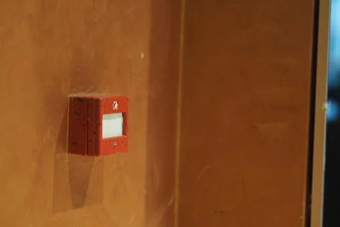 Small red button mounted on a wall in a simple indoor setting Stock Photos