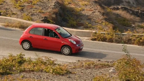 Small red car quickly appearing and driving down road behind hills, travel Stock Footage