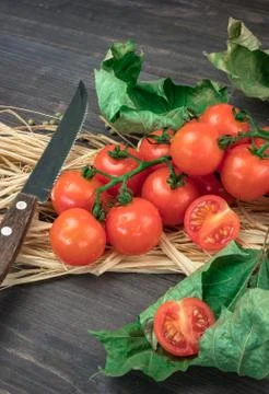 Small red cherry tomatoes on a branch, lying on a hay on an old wooden table Stock Photos