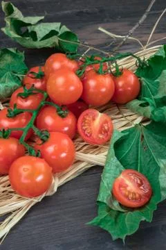 Small red cherry tomatoes on a branch, lying on a hay on an old wooden table  Stock Photos