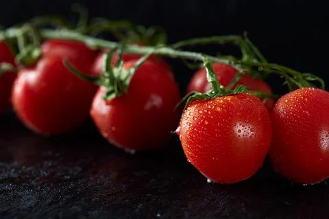 Small red cherry tomatoes on dark slate Stock Photos