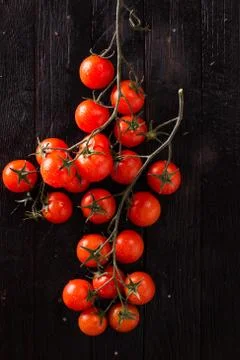 Small red cherry tomatoes on an old dark wooden table in rustic style Stock Photos