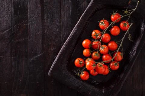 Small red cherry tomatoes on an old dark wooden table in rustic style Stock Photos