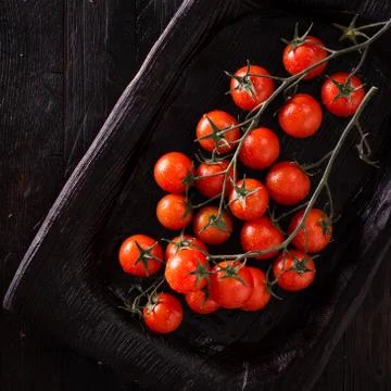 Small red cherry tomatoes on an old dark wooden table in rustic style Stock Photos