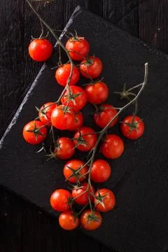 Small red cherry tomatoes on an old dark wooden table in rustic style Stock Photos
