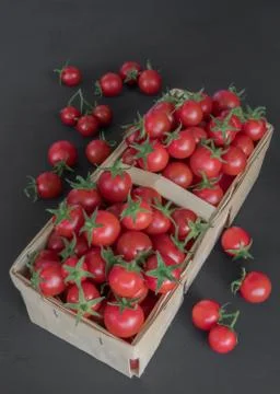 Small red cherry tomatoes in a wicker rattan basket on a wooden black backgro Stock Photos