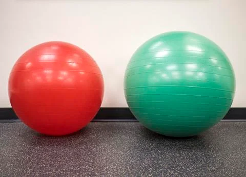 Small red exercise ball beside a medium size swiss ball in the gym Stock Photos