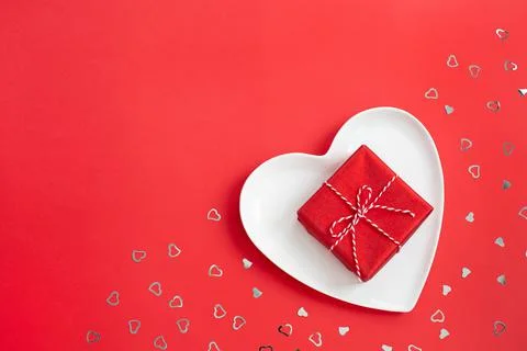 Small red gift box on a white heart-shaped plate. Stock Photos