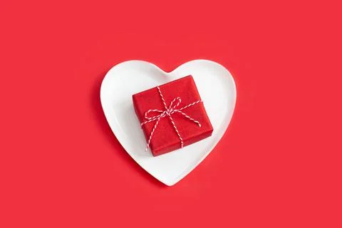 Small red gift box on a white heart-shaped plate. Stock Photos